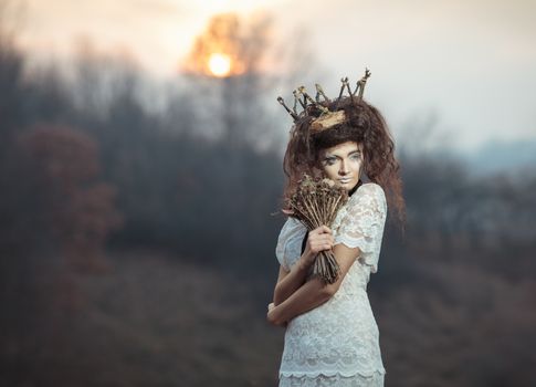 Young girl in the image of a bride in a white lace dress, a crown of twigs with a bouquet of dried flowers