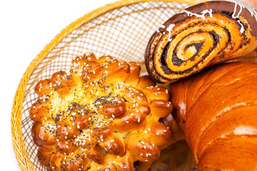 Fresh and tasty buns with with sesame and poppy seeds, bagel with jam and roll with chocolate in a basket over white background