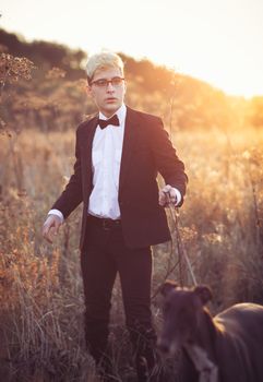 Young attractive man in suit and tie with a greyhound dog in autumn outdoors. He keeps the dog on the leash.