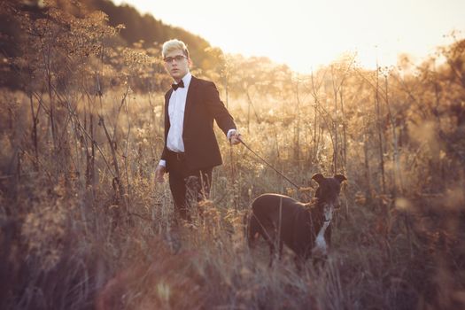 Young attractive man in suit and tie with a greyhound dog in autumn outdoors. He keeps the dog on the leash.