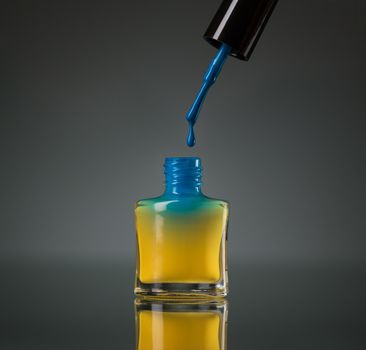 Flowing blue nail polish in the yellow bottle isolated on black