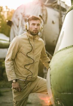 Young serious pilot posing near the helicopter