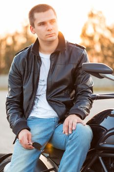 Biker man wearing a leather jacket and sunglasses sitting on his motorcycle outdoors