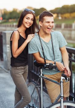 Happy couple - young smiling man and woman with bike in the park outdoor