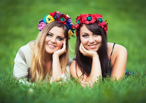 Two beautiful laughing girl in Ukrainian national costumes lie on the green grass