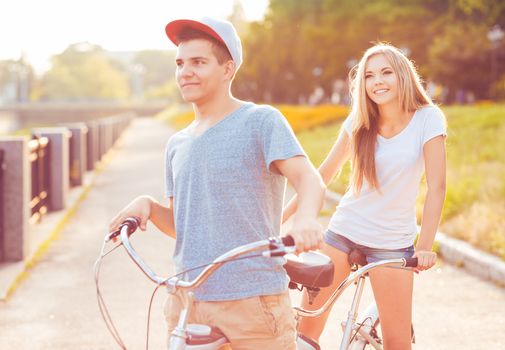 Happy couple - young man and woman riding a bicycle in the park outdoors