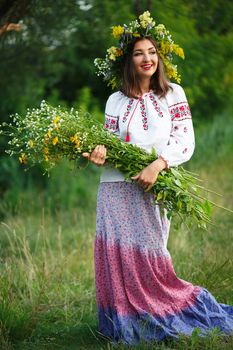 Young beautiful smiling girl in Ukrainian costume with a wreath on his head in a meadow