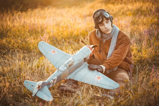 Young guy in vintage clothes pilot with an airplane model outdoors