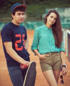 Young beautiful couple standing on a skateboard on the tennis court