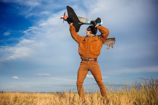 Young guy in vintage clothes pilot with an airplane model outdoors