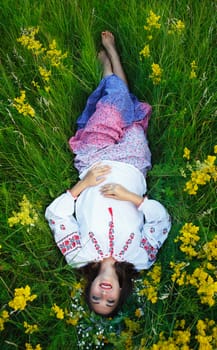 Young beautiful smiling girl in Ukrainian costume with a wreath on his head in a meadow