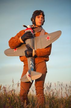 Young guy in vintage clothes pilot with an airplane model outdoors