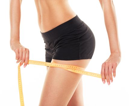 Closeup photo of a caucasian woman's leg. She is measuring her thigh with a yellow metric tape measure