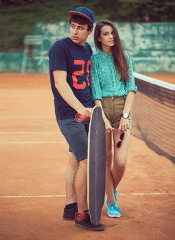 Young beautiful couple standing on a skateboard on the tennis court