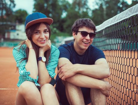 Young beautiful couple sitting on a skateboard on the tennis court