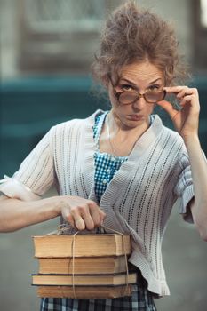Funny girl student with books in glasses and a vintage dress outdoors