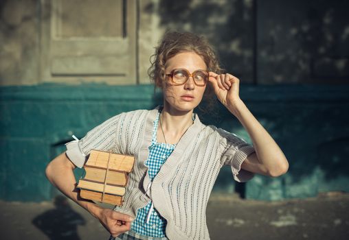Funny girl student with books in glasses and a vintage dress outdoors