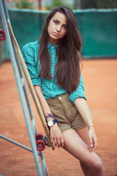 Beautiful young girl with longboard standing on the tennis court, outdoor