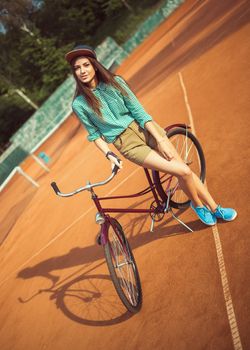 Girl hipster standing with magenta bike on the tennis court. Outdoor lifestyle portrait