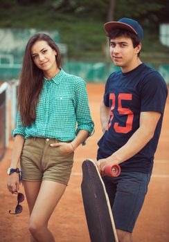Young beautiful couple standing on a skateboard on the tennis court