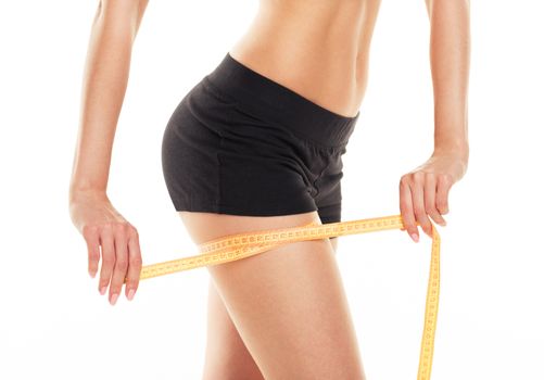 Closeup photo of a caucasian woman's leg. She is measuring her thigh with a yellow metric tape measure