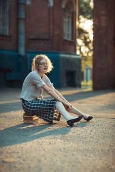 Funny crazy girl student with glasses sitting on a pile of books outdoor