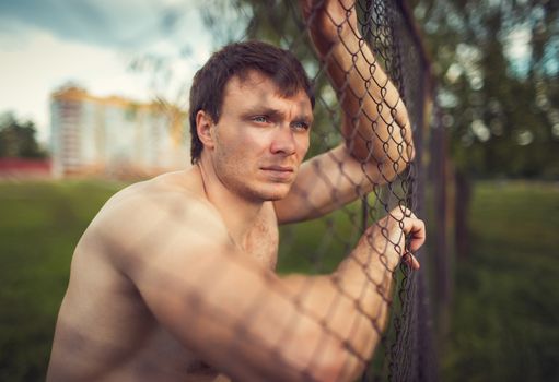 Young athletic guy near the netting in the outdoor