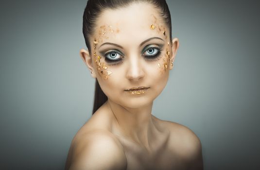 Glamorous portrait of young beautiful girl with big blue eyes, lush lashes and bright golden makeup. Fashion shiny highlighter on skin, velvet skin, gold lips