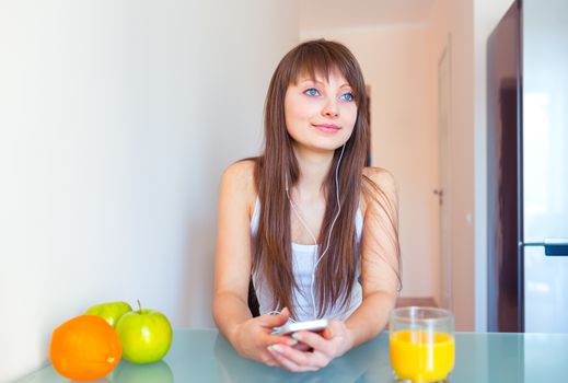 Young woman in the kitchen listening to music on headphones