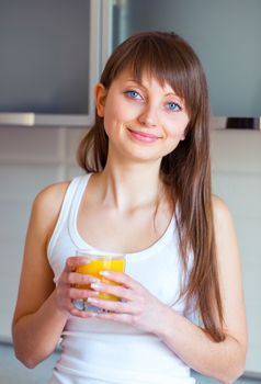 Young caucasian brunette girl with a glass of juice in the kitchen