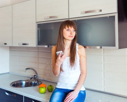 Young woman in the kitchen listening to music on headphones