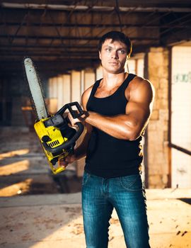 Muscular man with a chainsaw on the ruins