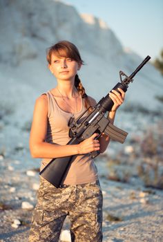 Young beautiful female soldier dressed in a camouflage with a gun in the outdoor