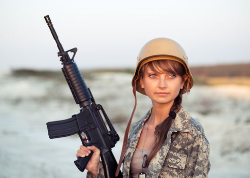 Young beautiful female soldier dressed in a camouflage with a gun in the outdoor