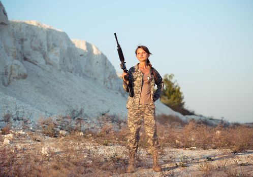 Young beautiful female soldier dressed in a camouflage with a gun in the location