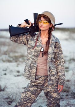 Young beautiful female soldier dressed in a camouflage with a gun in the outdoor