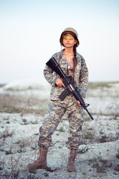 Young beautiful female soldier dressed in a camouflage with a gun in the outdoor