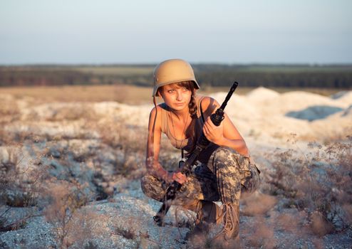 Young beautiful female soldier dressed in a camouflage with a gun in the outdoor