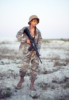 Young beautiful female soldier dressed in a camouflage with a gun in the outdoor