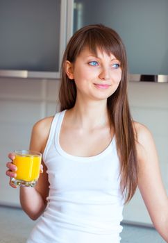 Young caucasian brunette girl with a glass of juice in the kitchen