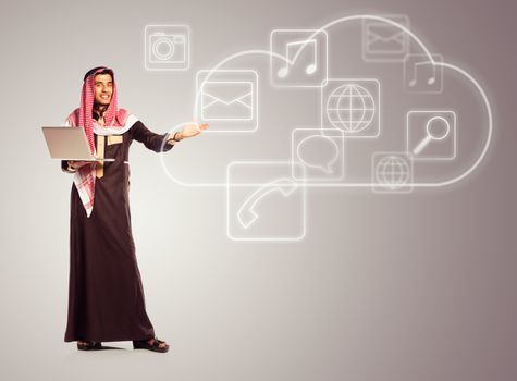 Young smiling arab with laptop shows virtual icons of the cloud service. Multimedia concept