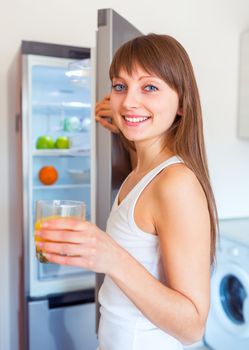 Young caucasian brunette girl with a glass of juice near the refrigerator