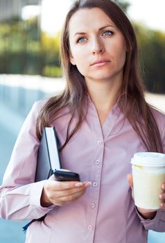 Young businesswoman with cellphone and organizer while standing against office building, outdoor