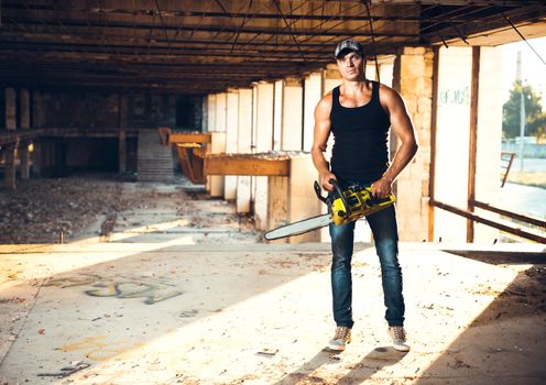 Muscular man with a chainsaw on the ruins