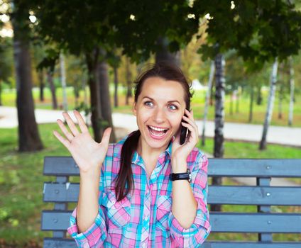 A portrait of a smiling beautiful woman in a park on a bench talking on the phone