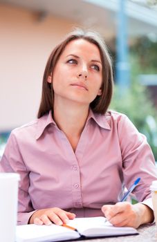 Thoughtful businesswoman sitting in a cafe and writing in notepad