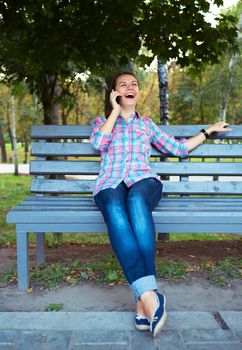 A portrait of a smiling beautiful woman in a park on a bench talking on the phone