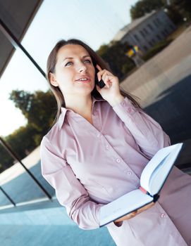 Young businesswoman with cellphone and organizer while standing against office building, outdoor