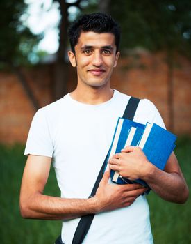 Arab male student with books outdoors looking very happy