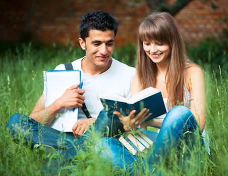 Two students guy and girl studying in park on grass with book outdoors